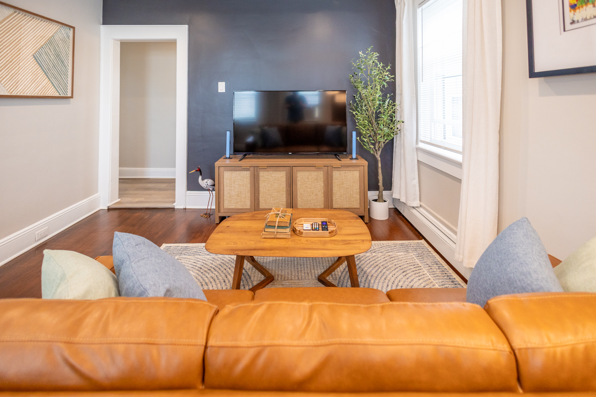 A living room with a leather sofa facing a flat-screen TV on a wooden console, with a coffee table and rug in front.