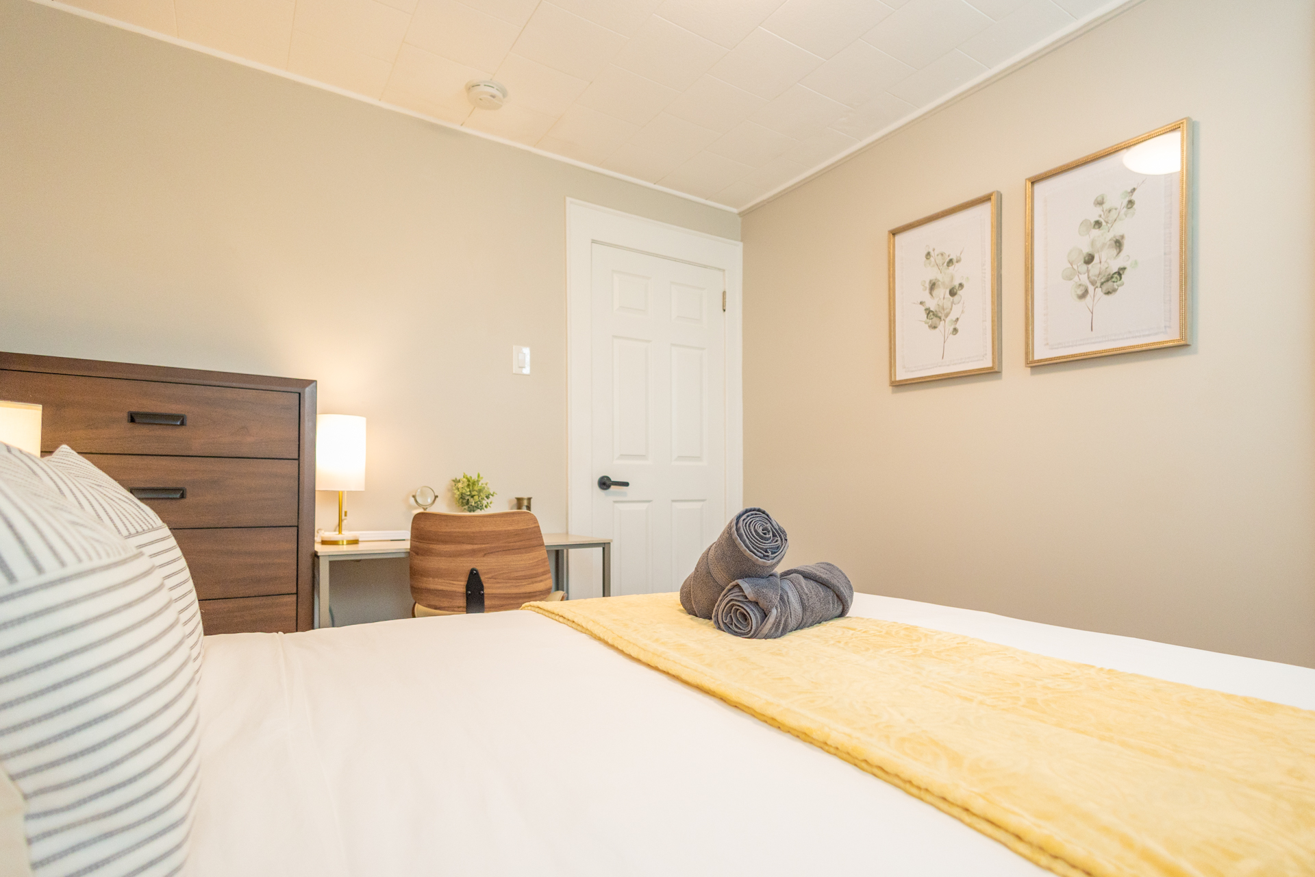 A bedroom corner with a wooden desk, modern chair, lamp, and small decorative touches, next to a tall dresser.