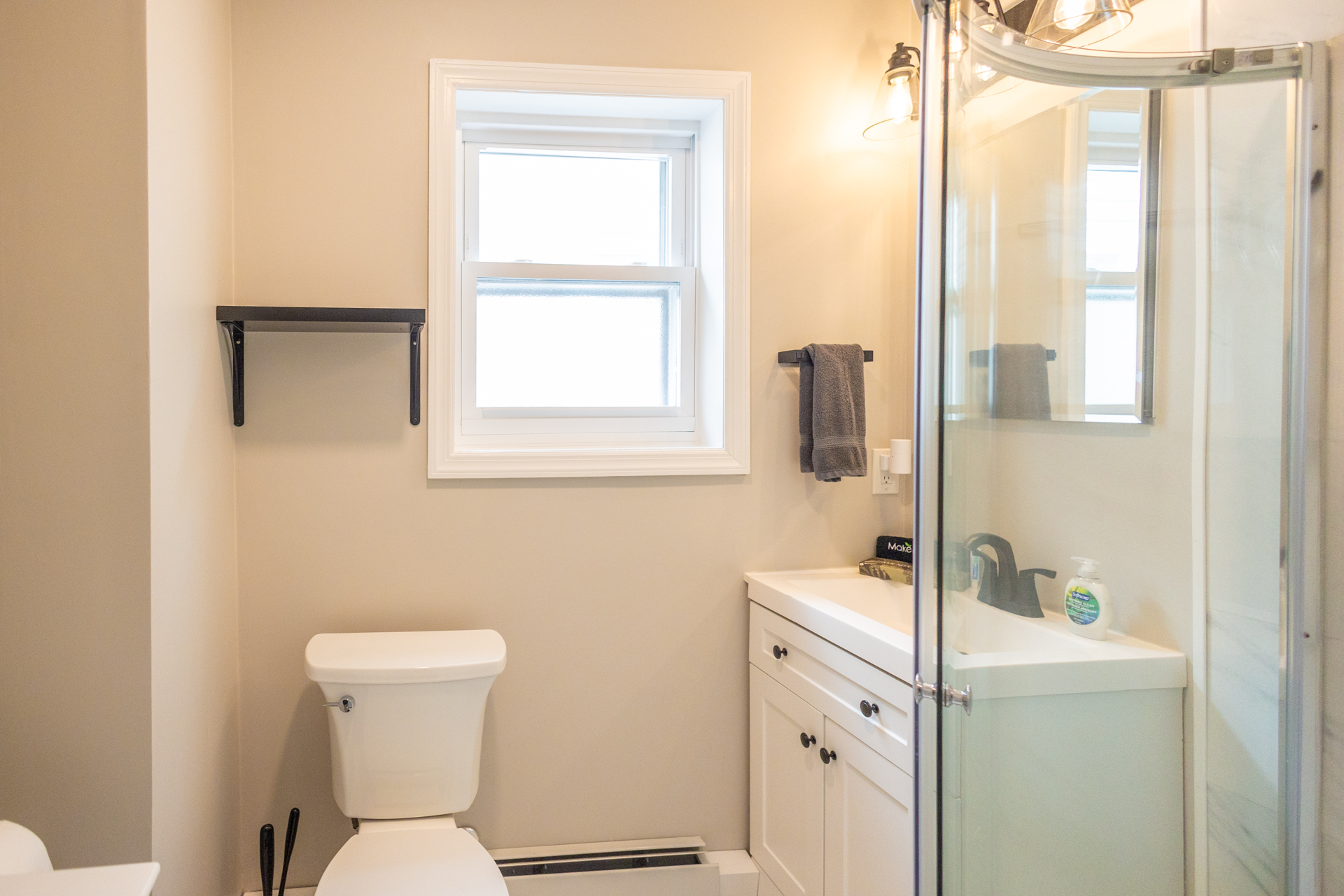 Bathroom with white toilet, vanity sink, and corner glass shower under a frosted window.