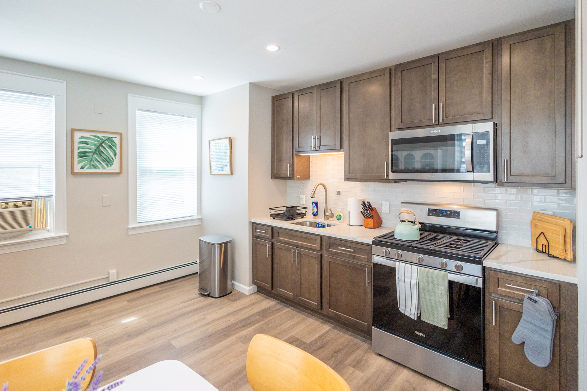 A wide view of the kitchen showing cabinets, stove, microwave, sink, and bright windows letting in natural light.
