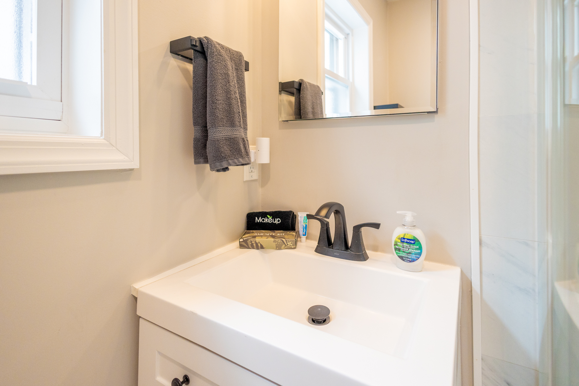 White vanity sink with black faucet, hand soap, and amenities like a makeup kit and toothbrush set.