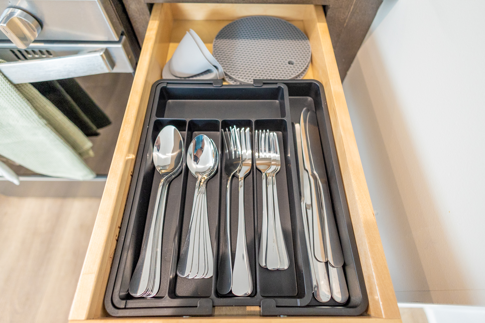 Drawer with neatly organized forks, knives, and spoons in a black tray.