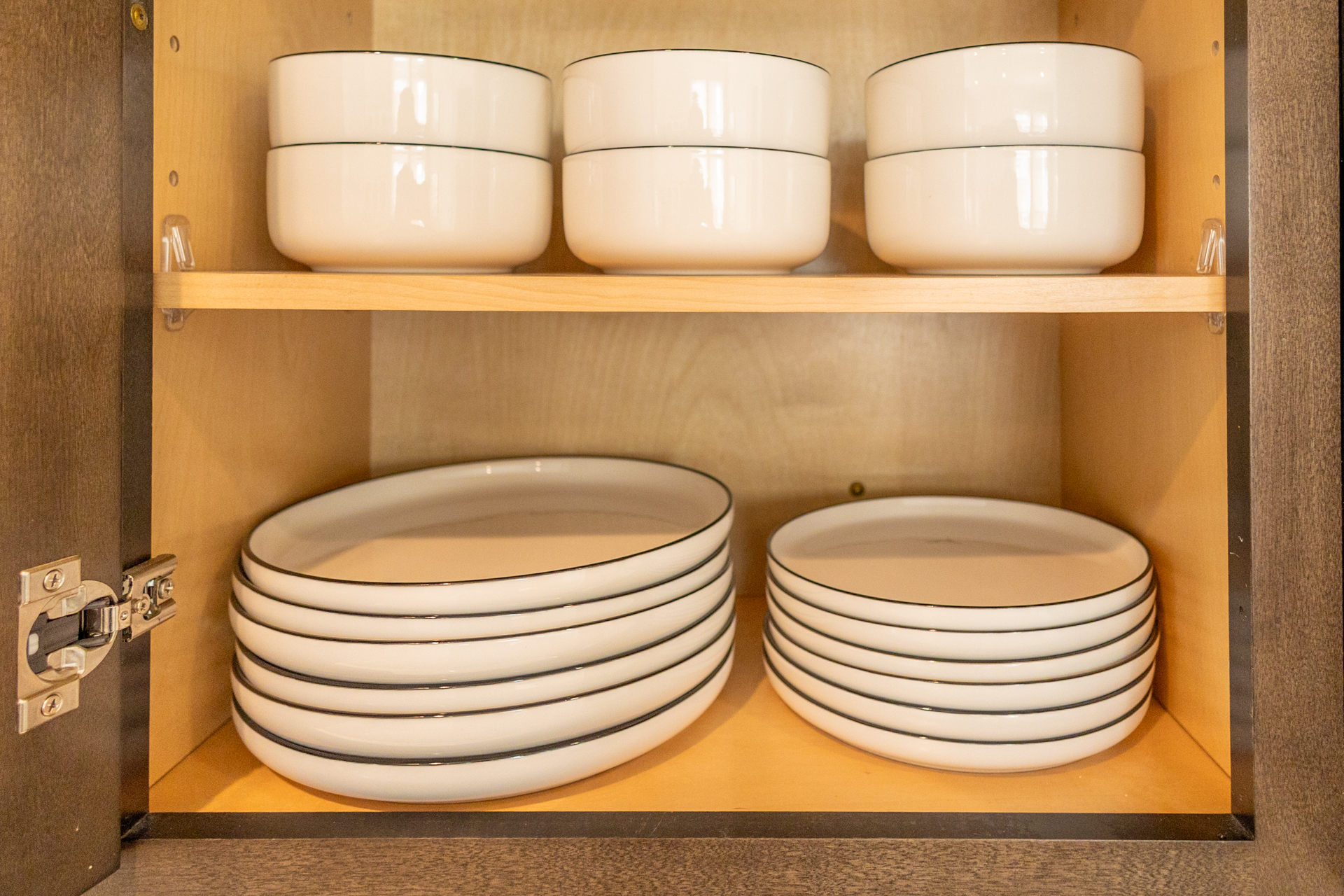 Open cabinet with a stack of white dinner plates, salad plates, and matching bowls.