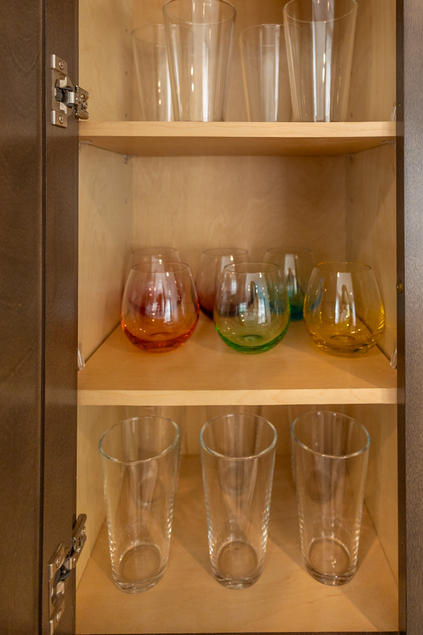 Oak2-39 Cabinet with assorted drinking glasses — tall pint glasses, clear tumblers, and colorful stemless glasses.