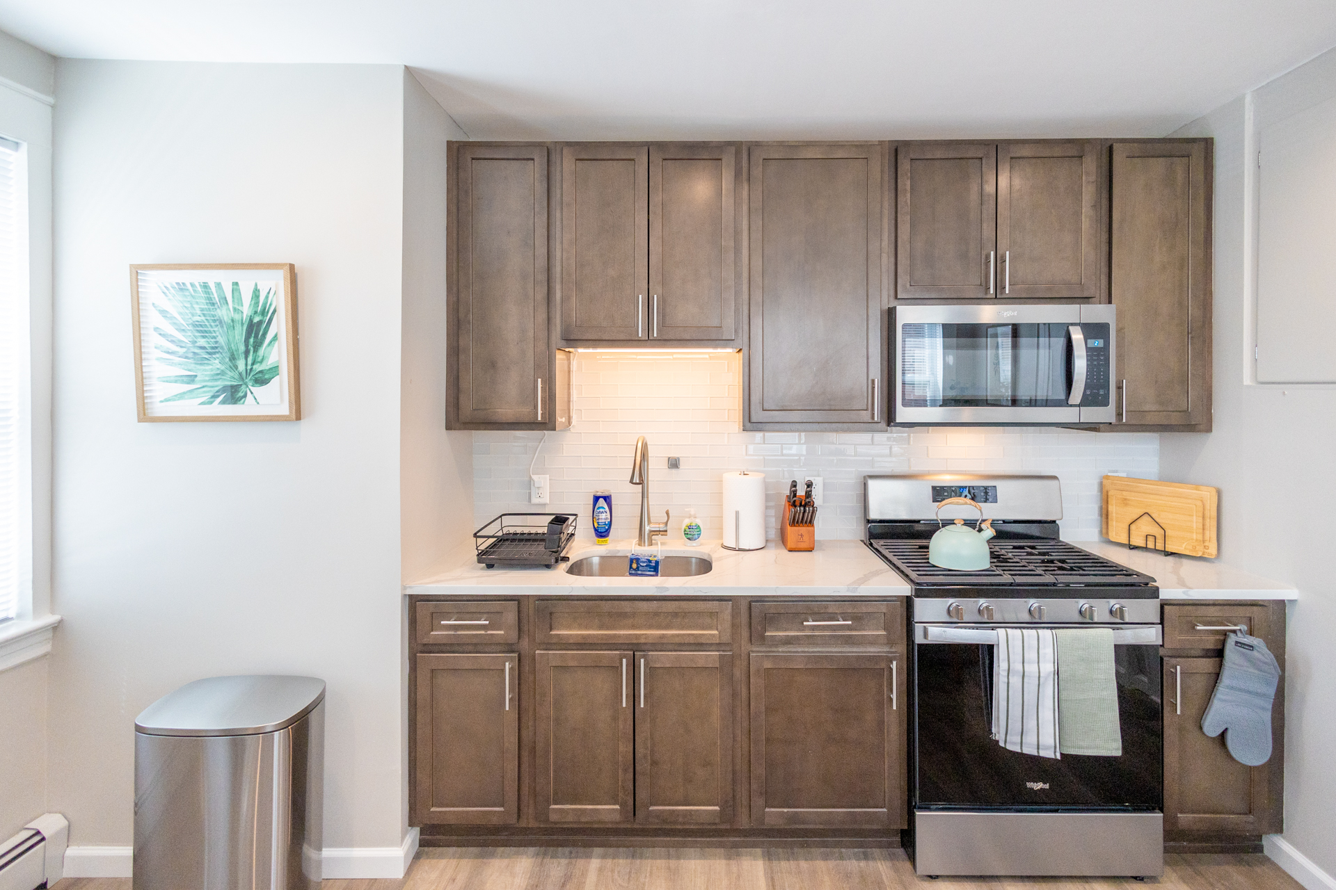 A clean kitchen counter with a sink, dish rack, paper towel holder, knife block, and stainless steel appliances.