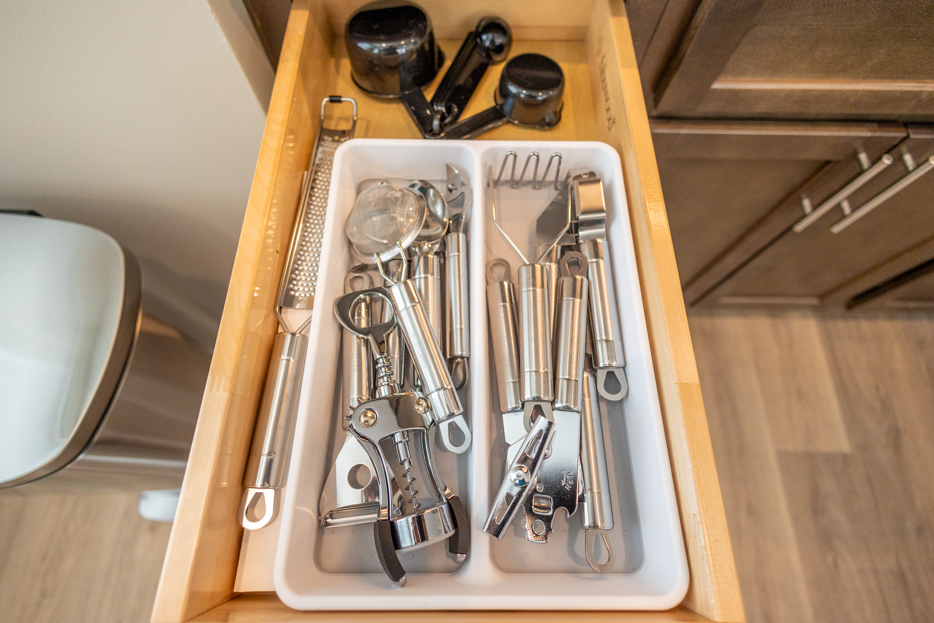 Drawer with stainless steel utensils including corkscrew, garlic press, zester, can opener, and measuring spoons