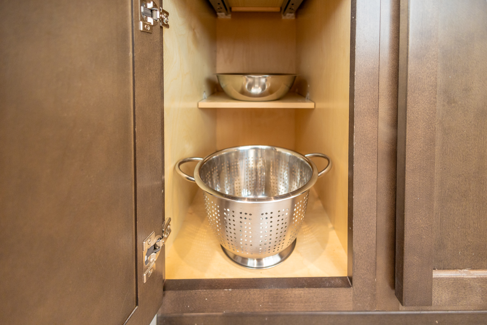 Cabinet with a large stainless steel colander and metal mixing bowl