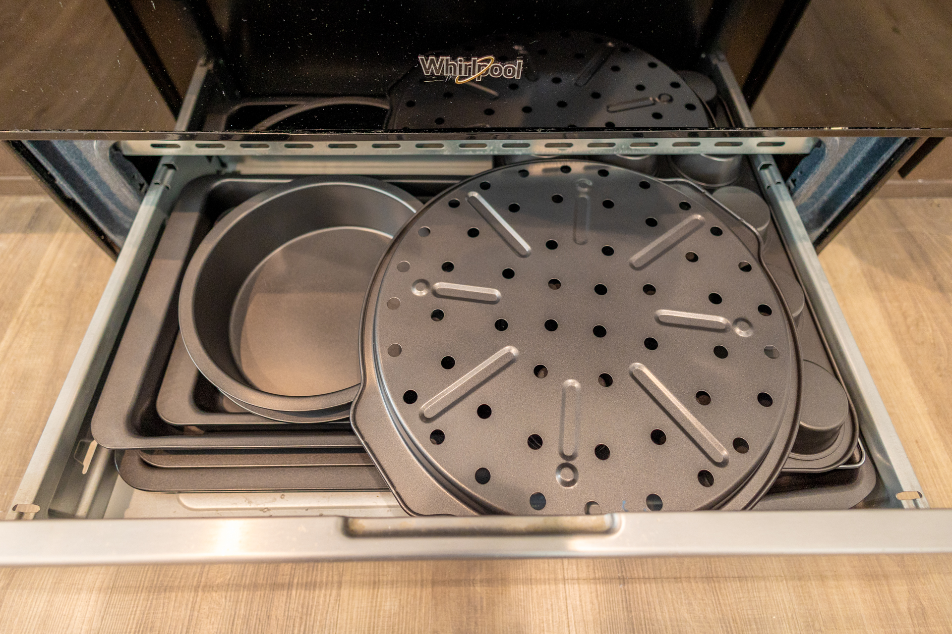 Oven drawer filled with baking pans, pizza tray, and cake pans.