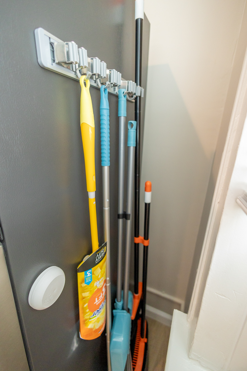 Wall-mounted organizer holding broom, mop, and dustpan neatly stored.