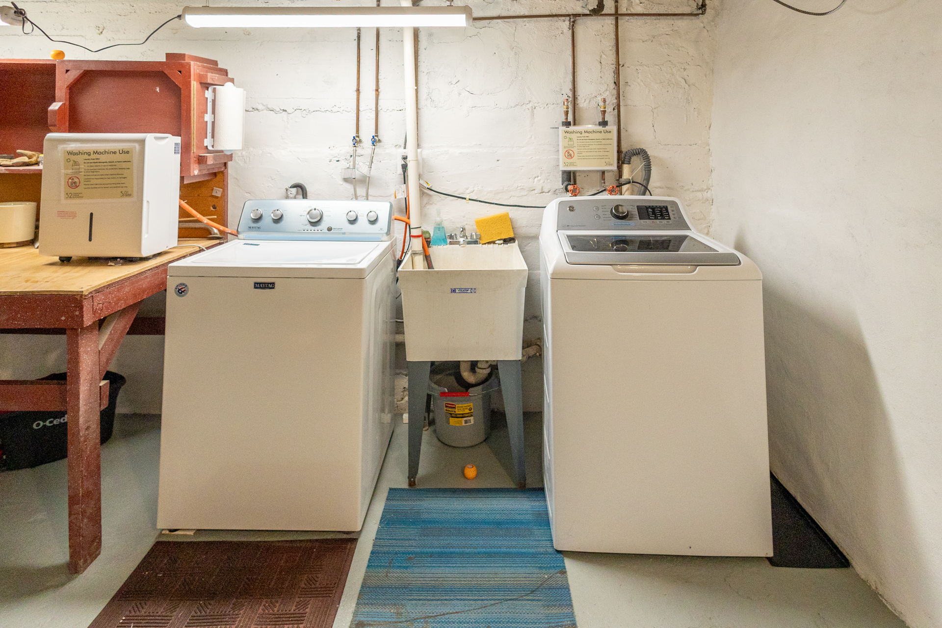 Basement laundry area with two washers, a dryer, and a utility sink between them