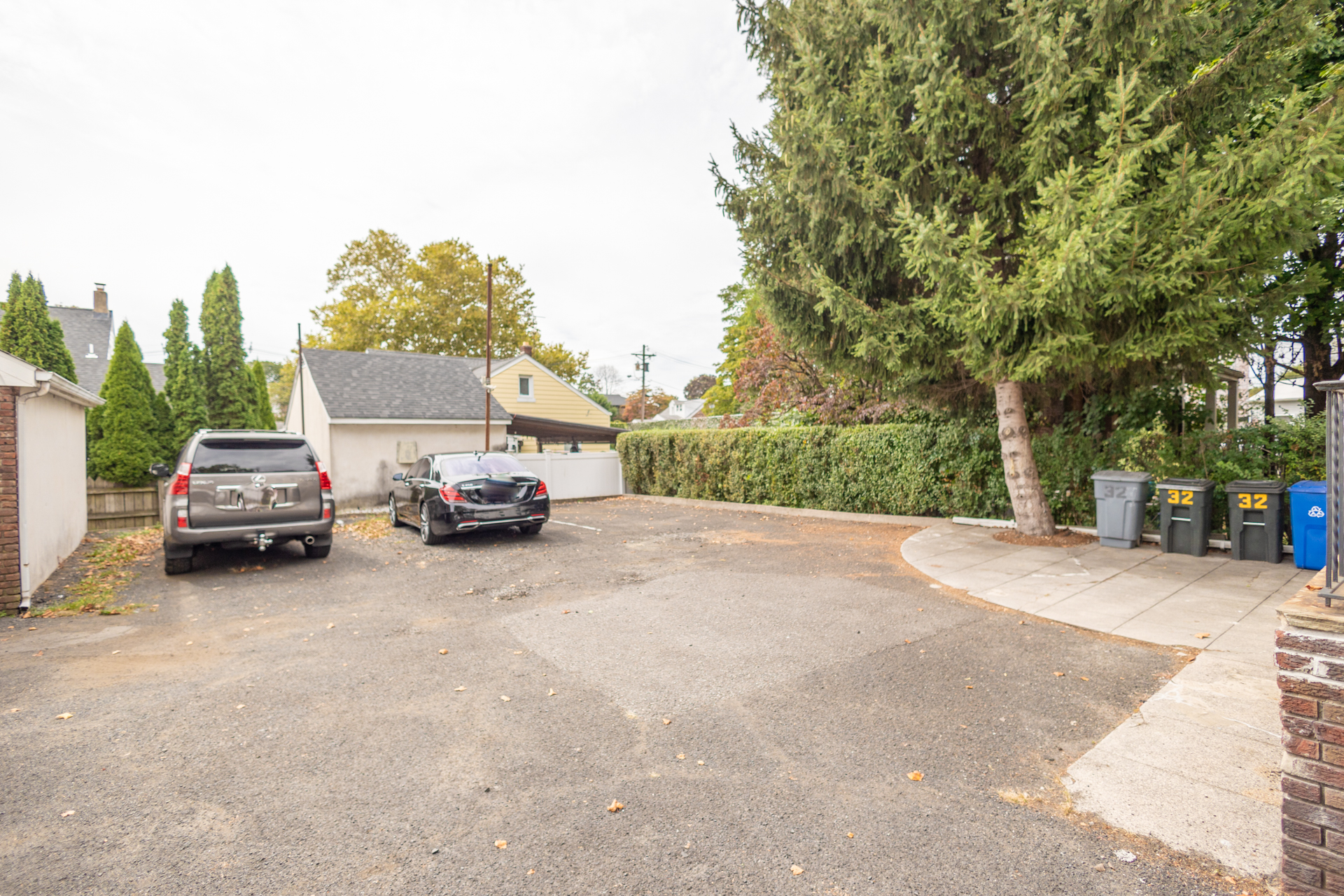 Outdoor parking lot with two cars, garbage bins lined on the right, and space for multiple vehicles.