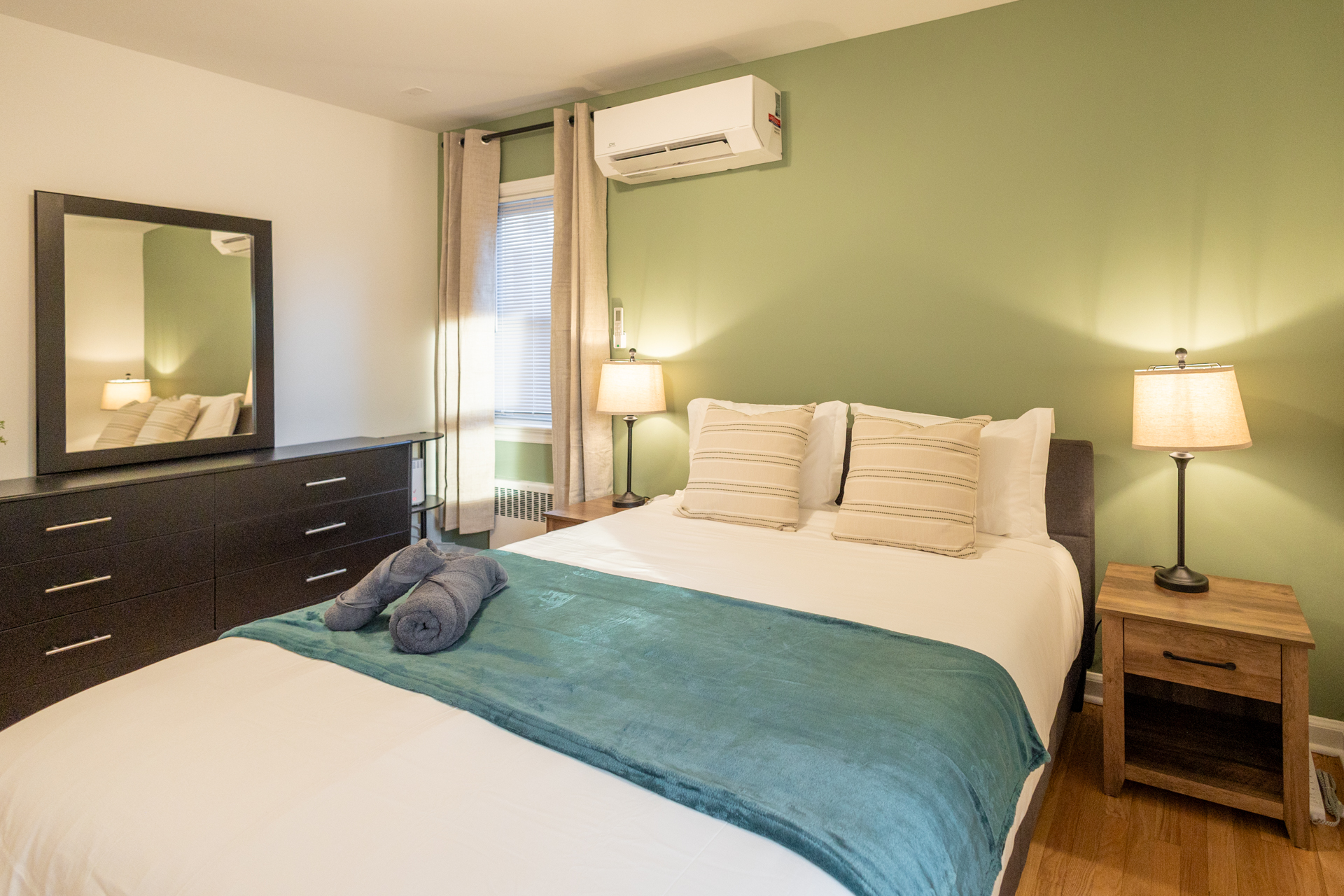 Calming bedroom with green and beige décor, twin bed, bedside lamps, chandelier, and window light.