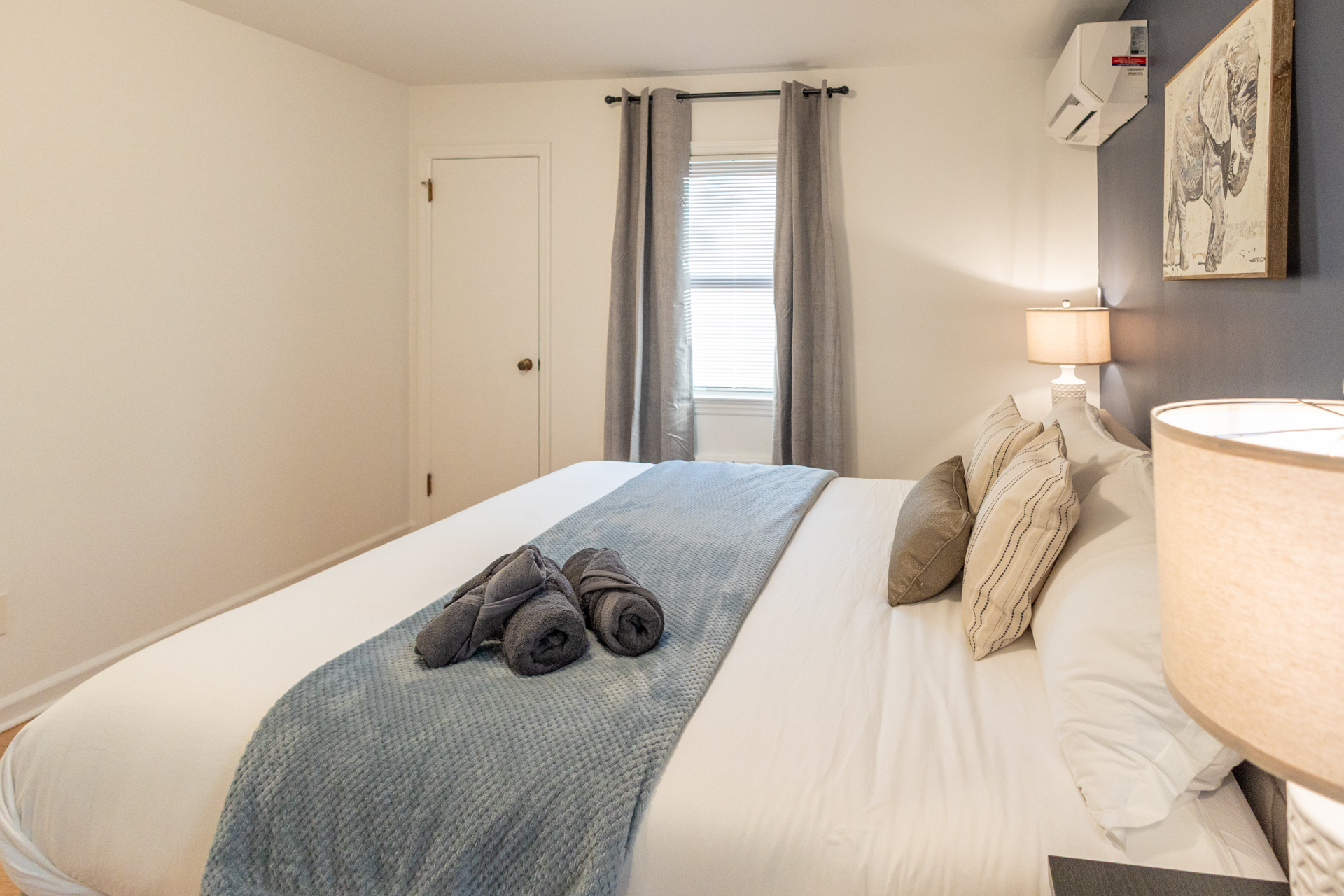 Bedroom with a large bed as the focal point, dressed in white linens and adorned with a blue textured throw blanket and neatly rolled gray towels.
