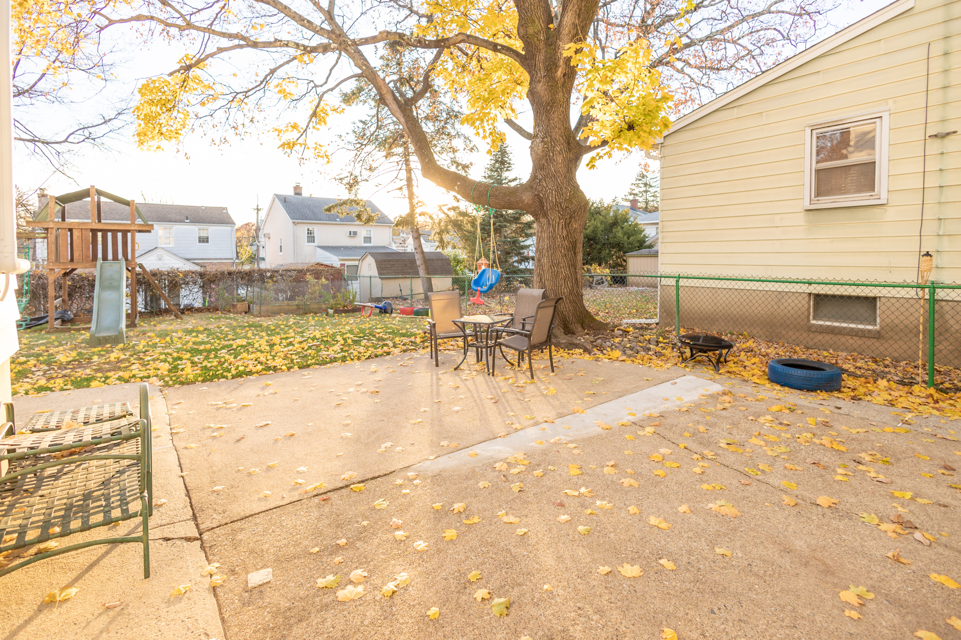 Suburban backyard with tree, patio table and chair, fence, and grill.