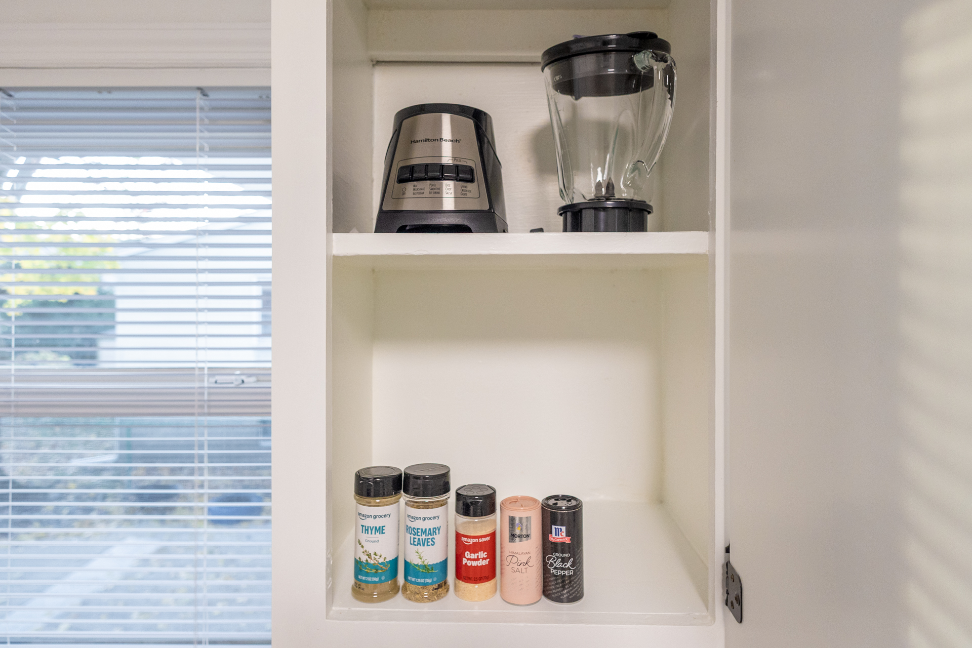 Kitchen cabinet featuring Hamilton Beach blender and assorted spices.