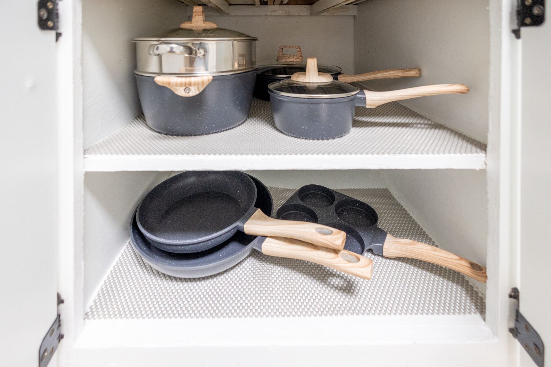 Neatly organized kitchen cabinet with pots and pans on three shelves.