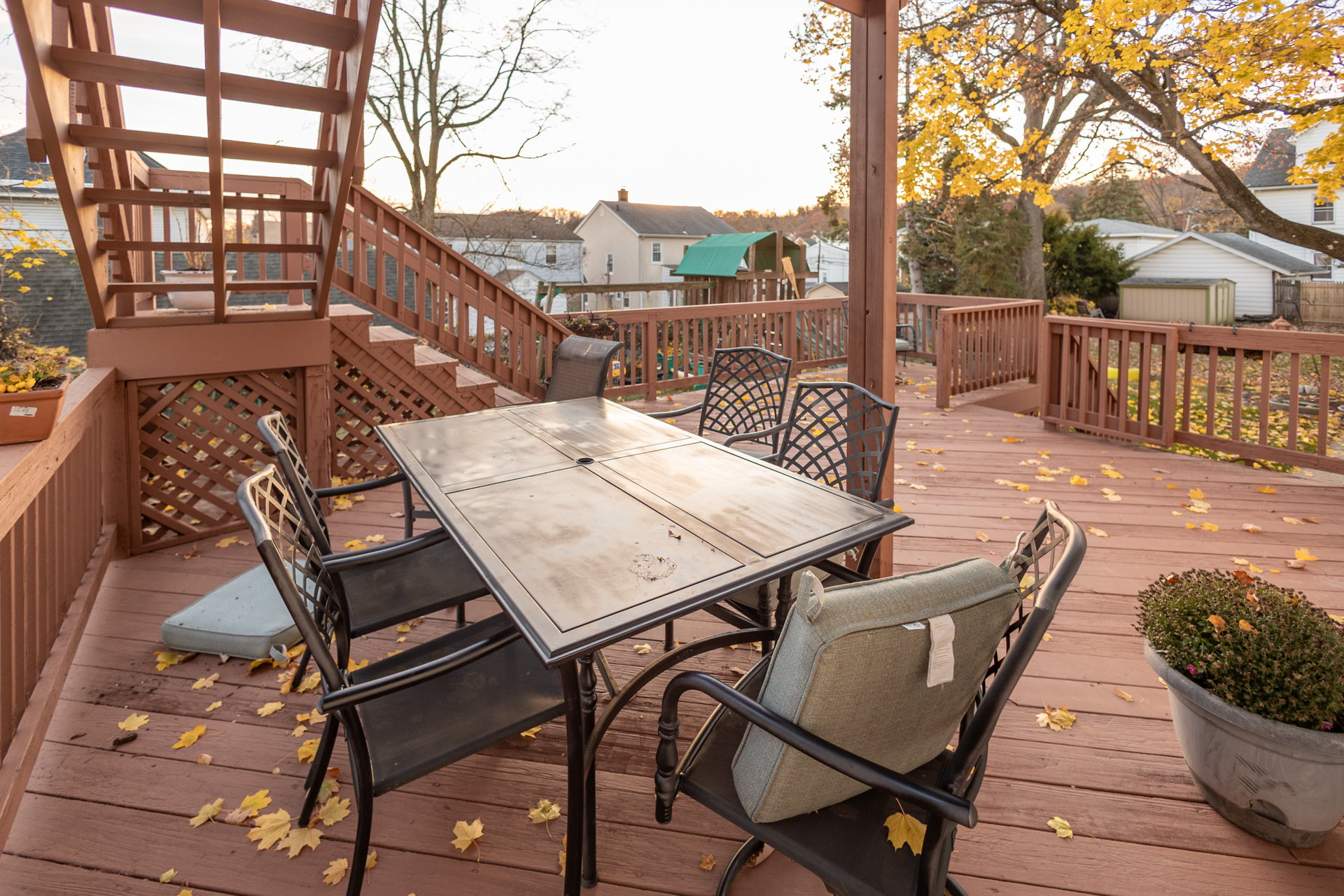 Cozy sunlit outdoor patio with glass table, four chairs, and wooden deck.