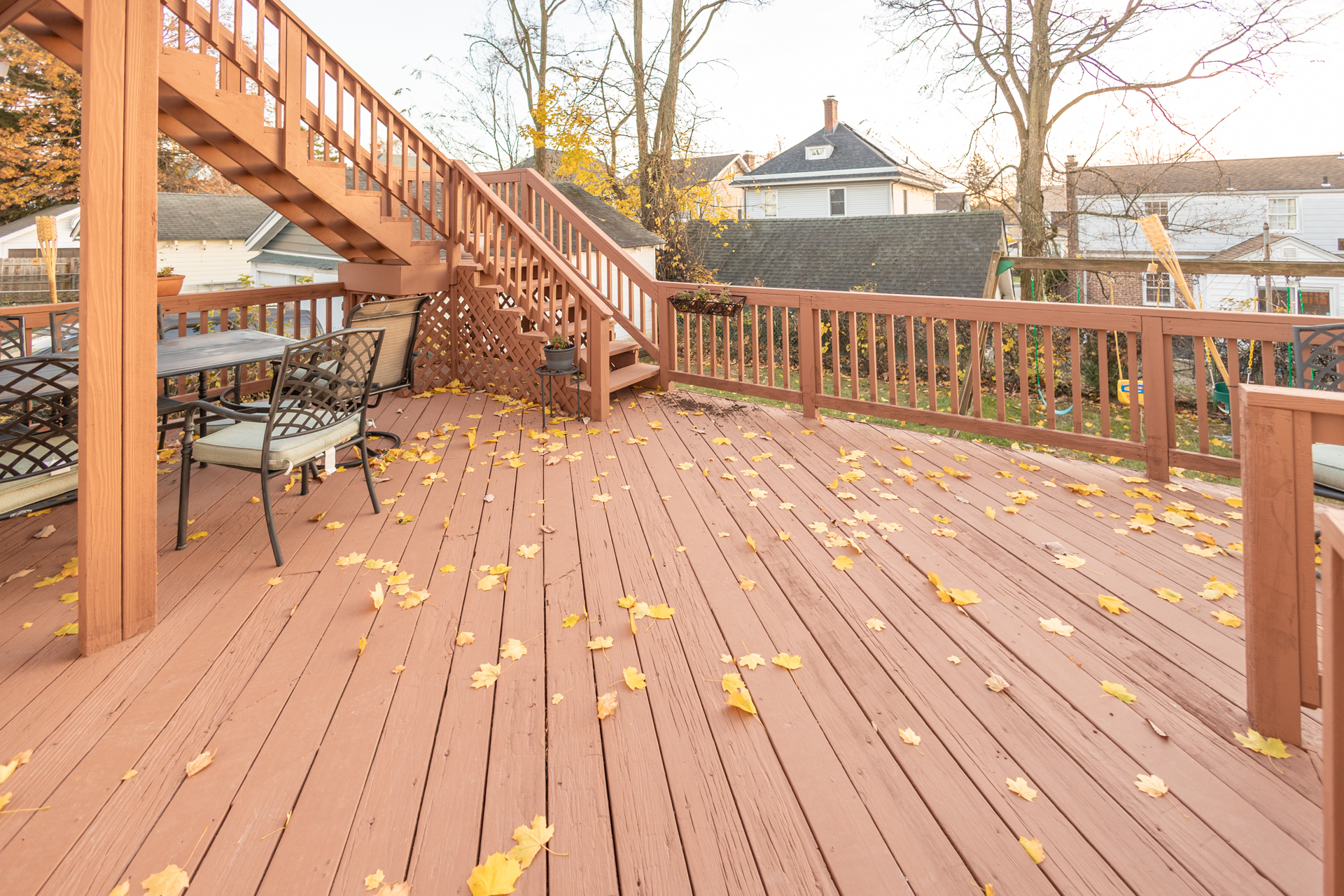 Wooden staircase with a lattice railing leading to a small porch area. On the left side, there are two black metal chairs with cushioned seats.