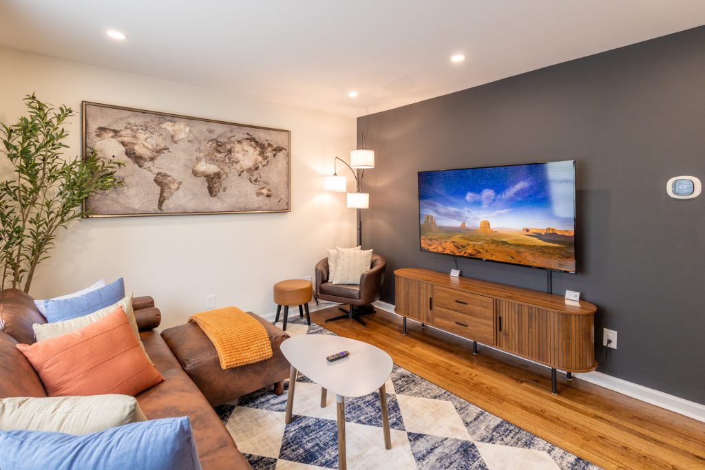 Modern living room with sectional sofa, mounted Smart TV, accent chair, coffee table, and world map wall art.