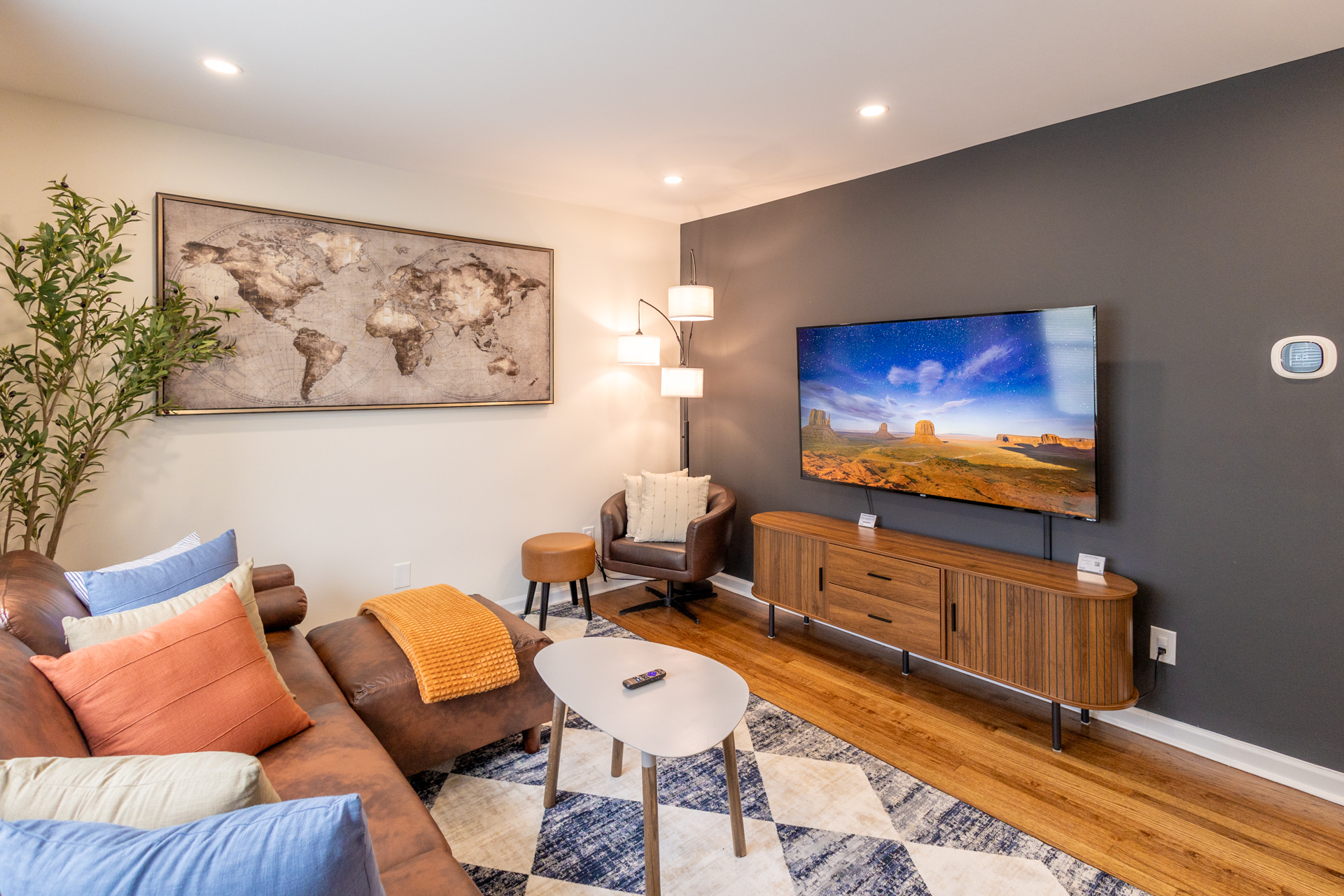 Modern living room with sectional sofa, mounted Smart TV, accent chair, coffee table, and world map wall art.