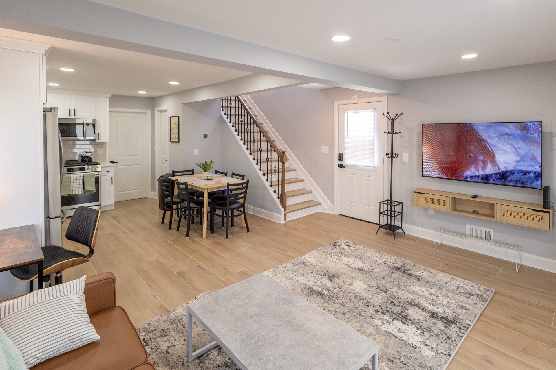 Open-concept living area with a sofa, coffee table, dining space, kitchen, and staircase.