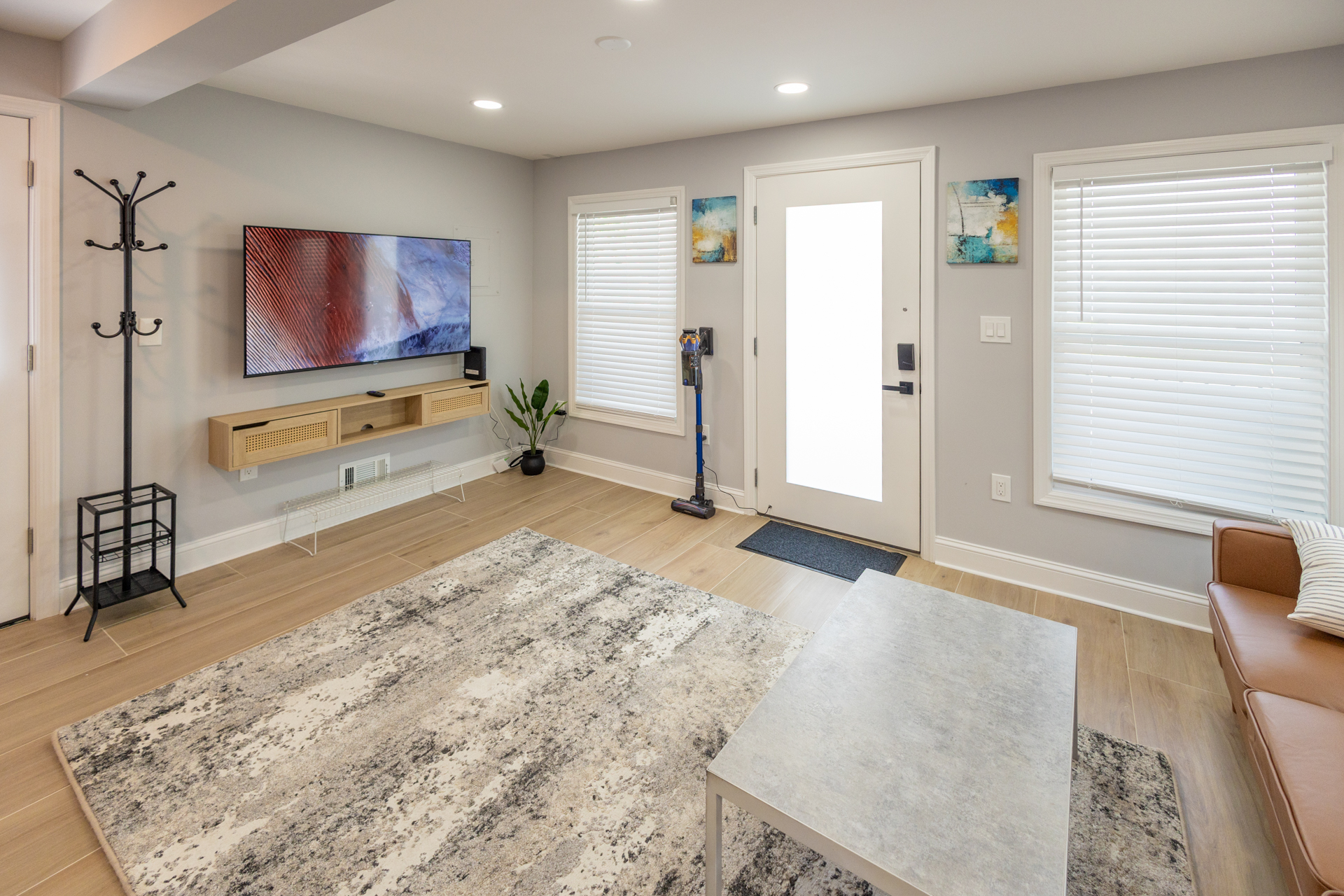Bright living room with a wall-mounted TV, modern coffee table, area rug, and large windows.