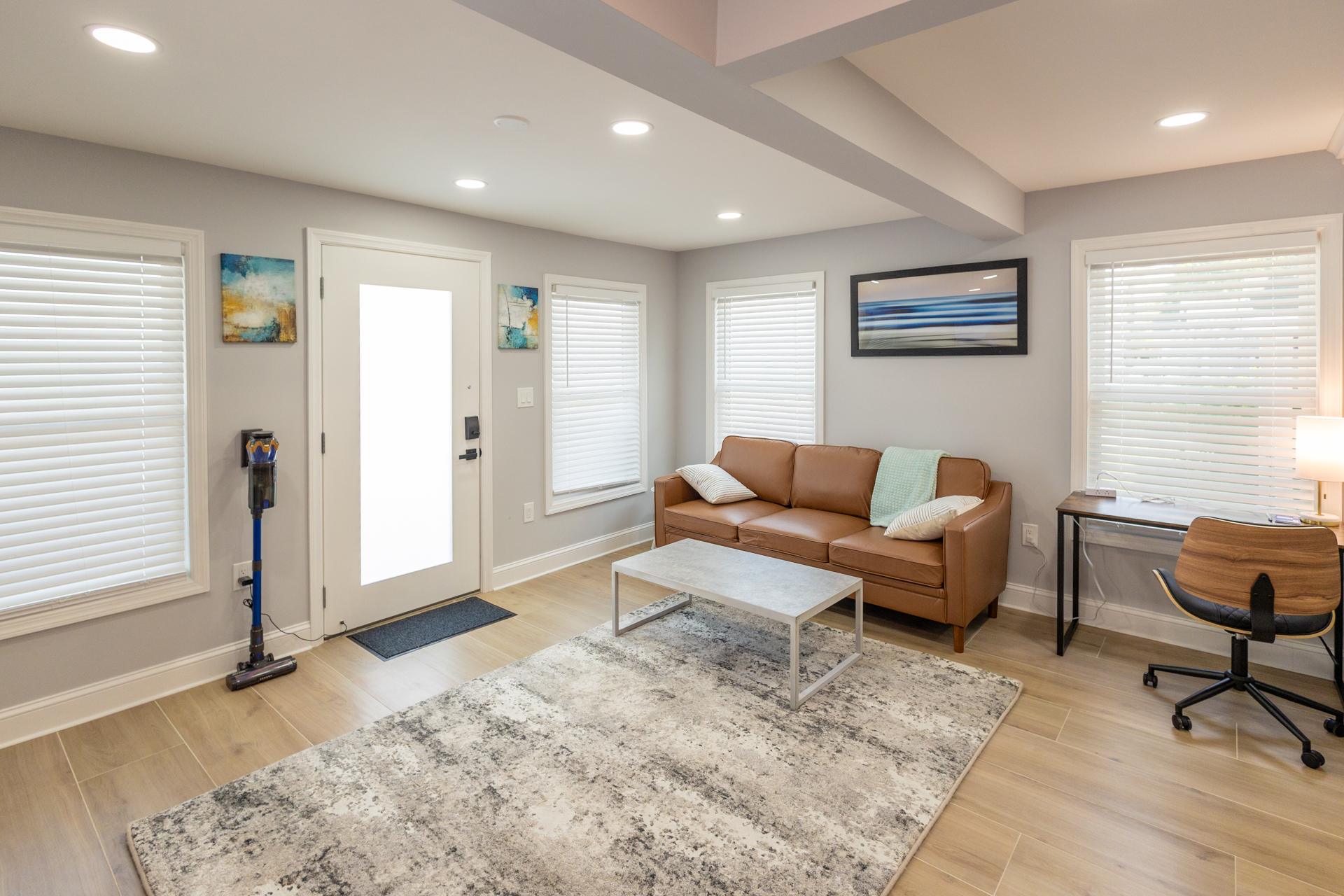 Bright living room with a comfortable sofa, home office desk, large windows, and a welcoming entryway.