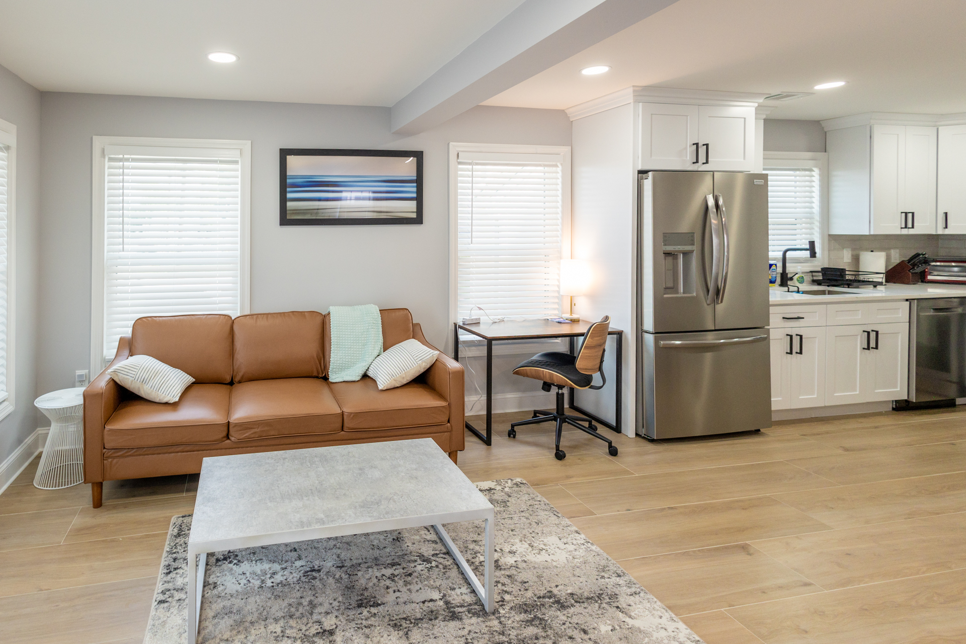 Open-concept living room and kitchen with a sofa, coffee table, workspace, and modern appliances.