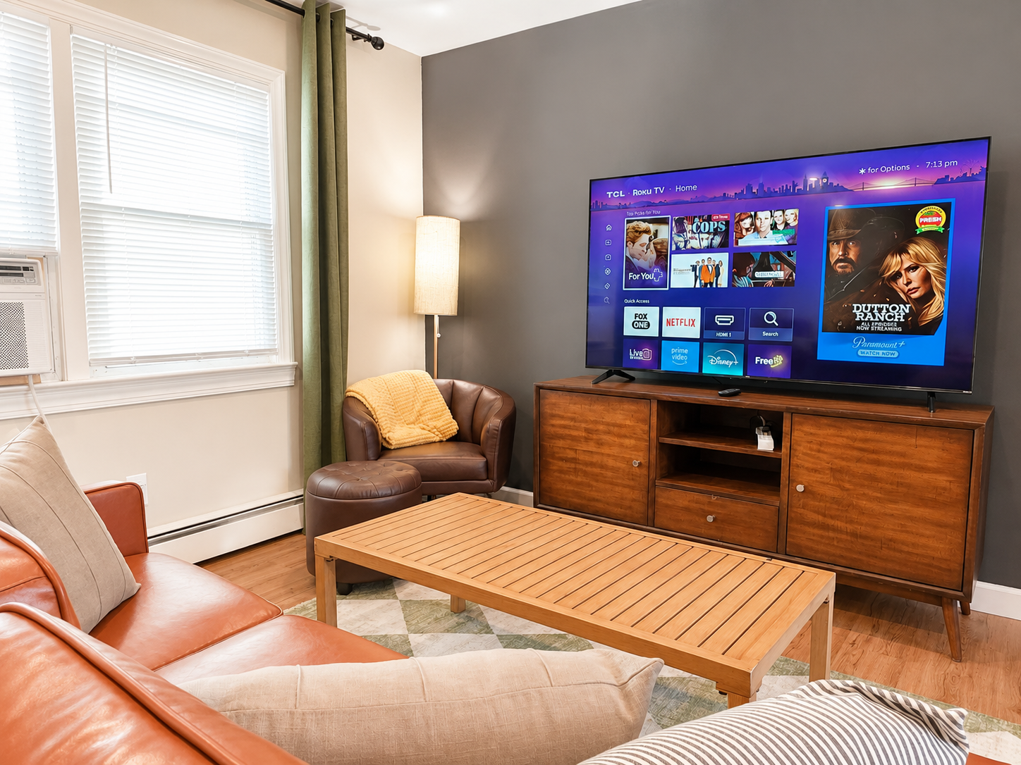 Cozy furnished living room with a leather armchair, sofa, wooden coffee table, TV, and warm lighting.