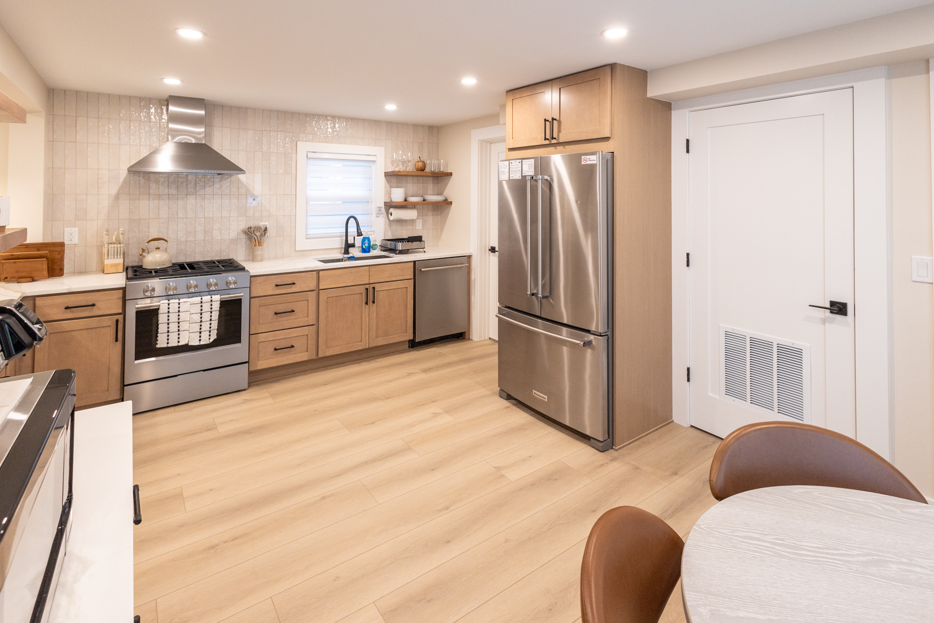 Modern kitchen with stainless steel appliances, wood cabinetry, and a dining area with four chairs.