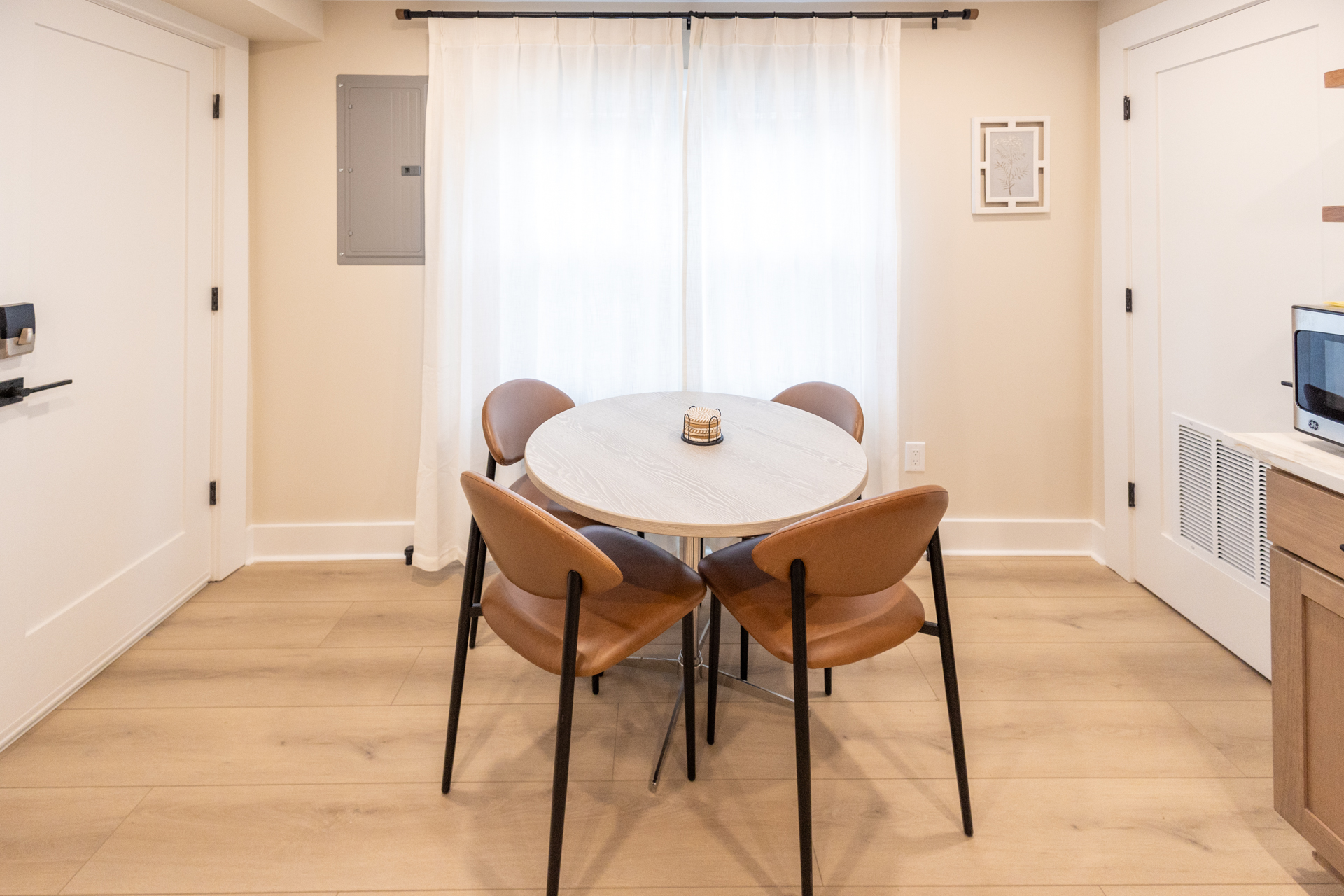 Dining area with a round table, four chairs, and large windows providing natural light.