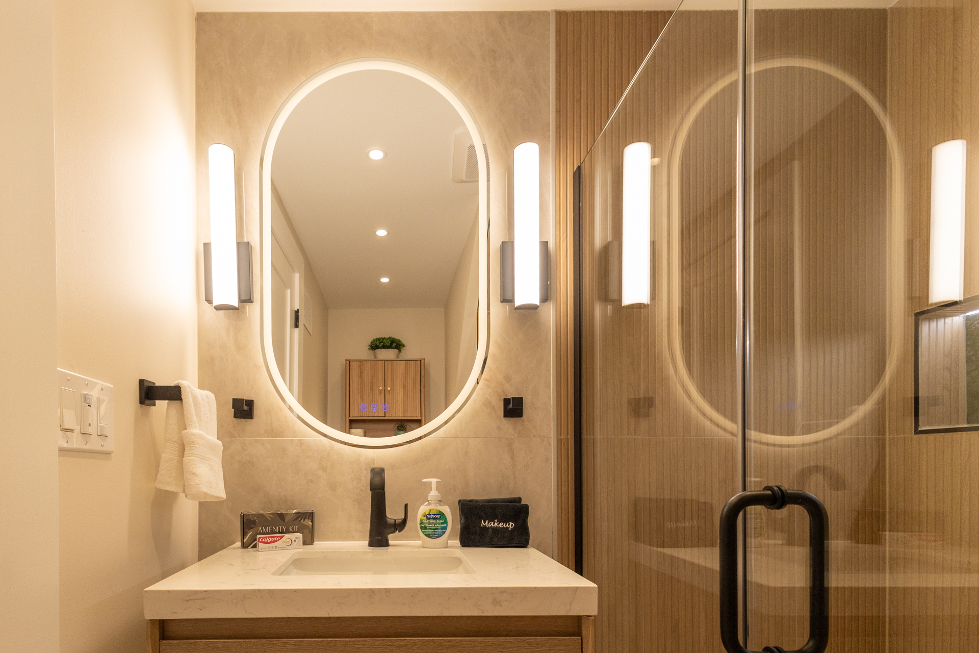 Modern bathroom with a white vanity, illuminated arched mirror, and glass-enclosed shower.
