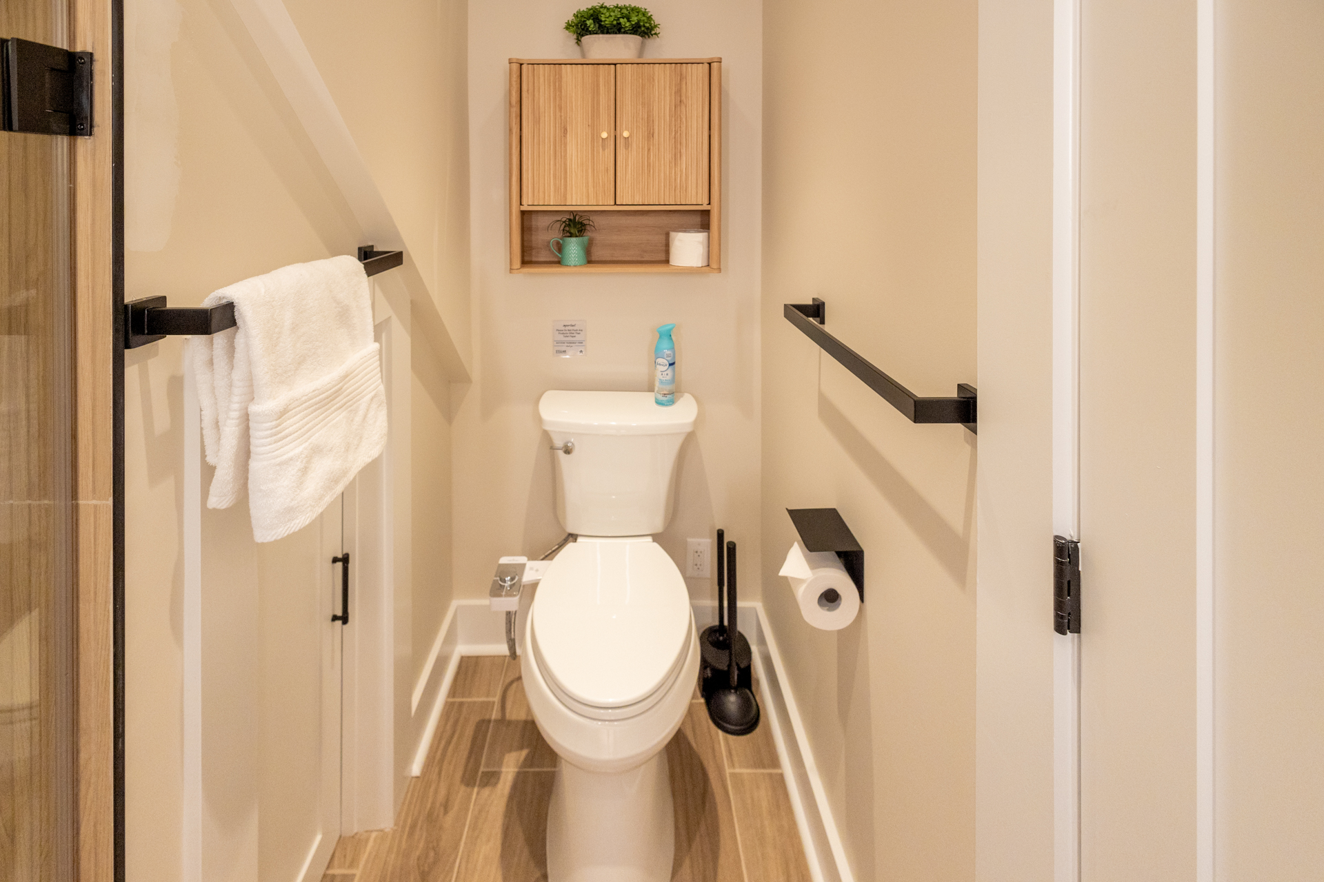 Small bathroom with a toilet, wall shelves, towel rack, and wood-look flooring.