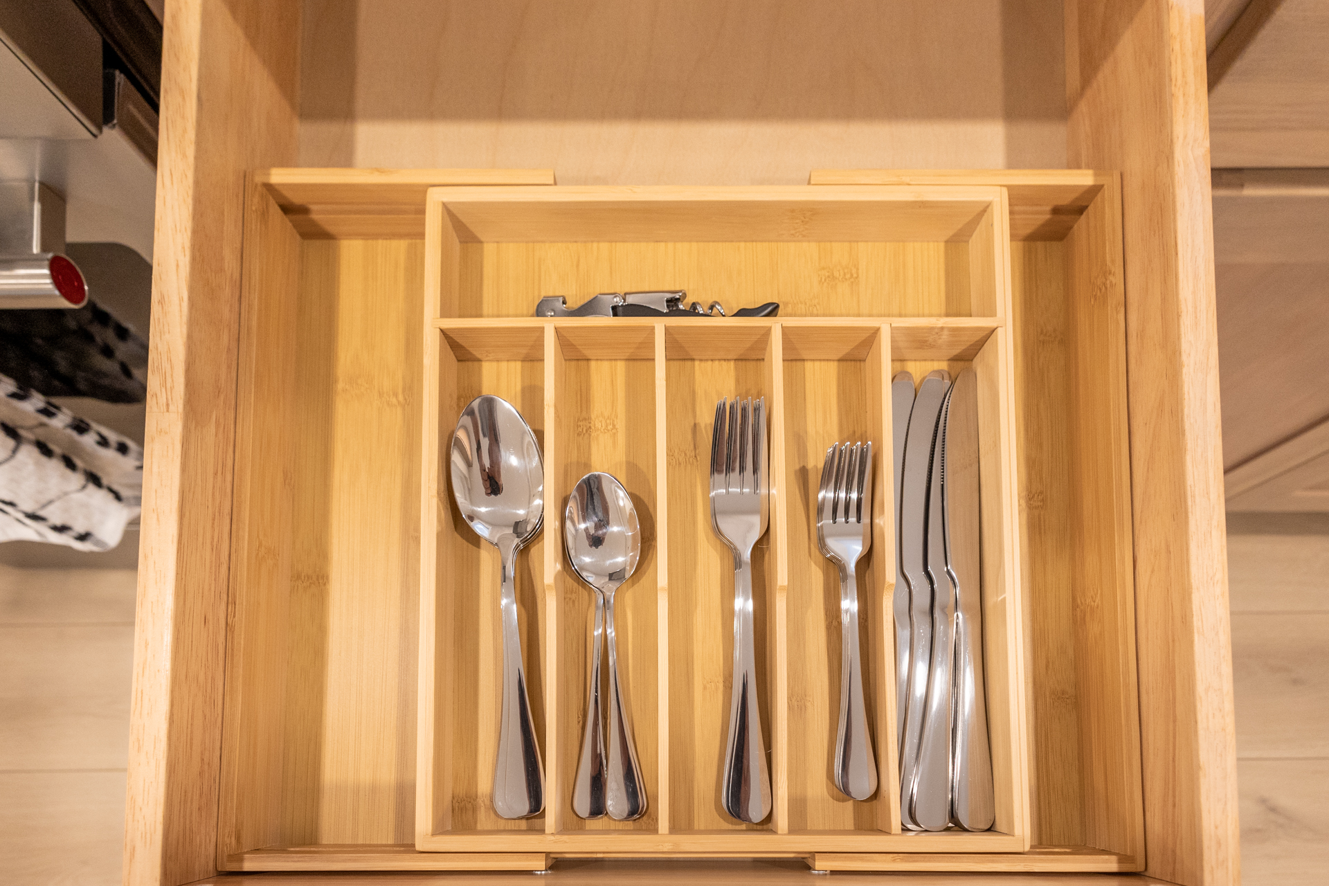 Wooden drawer containing organized spoons, forks, knives, and serving utensils.