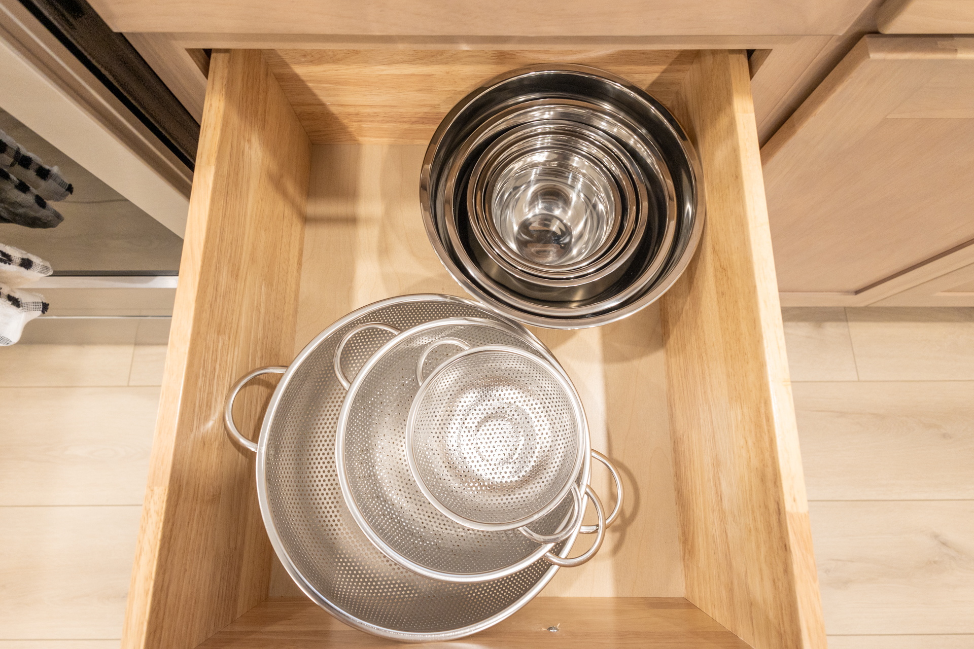 Cabinet shelf containing stacked metal bowls, colanders, and kitchen strainers.