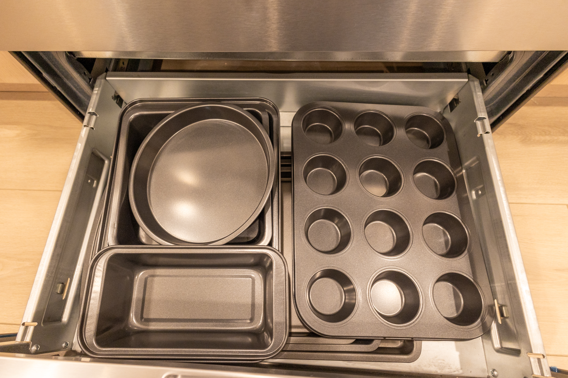 Open kitchen drawer neatly organized with baking pans and a muffin tin.