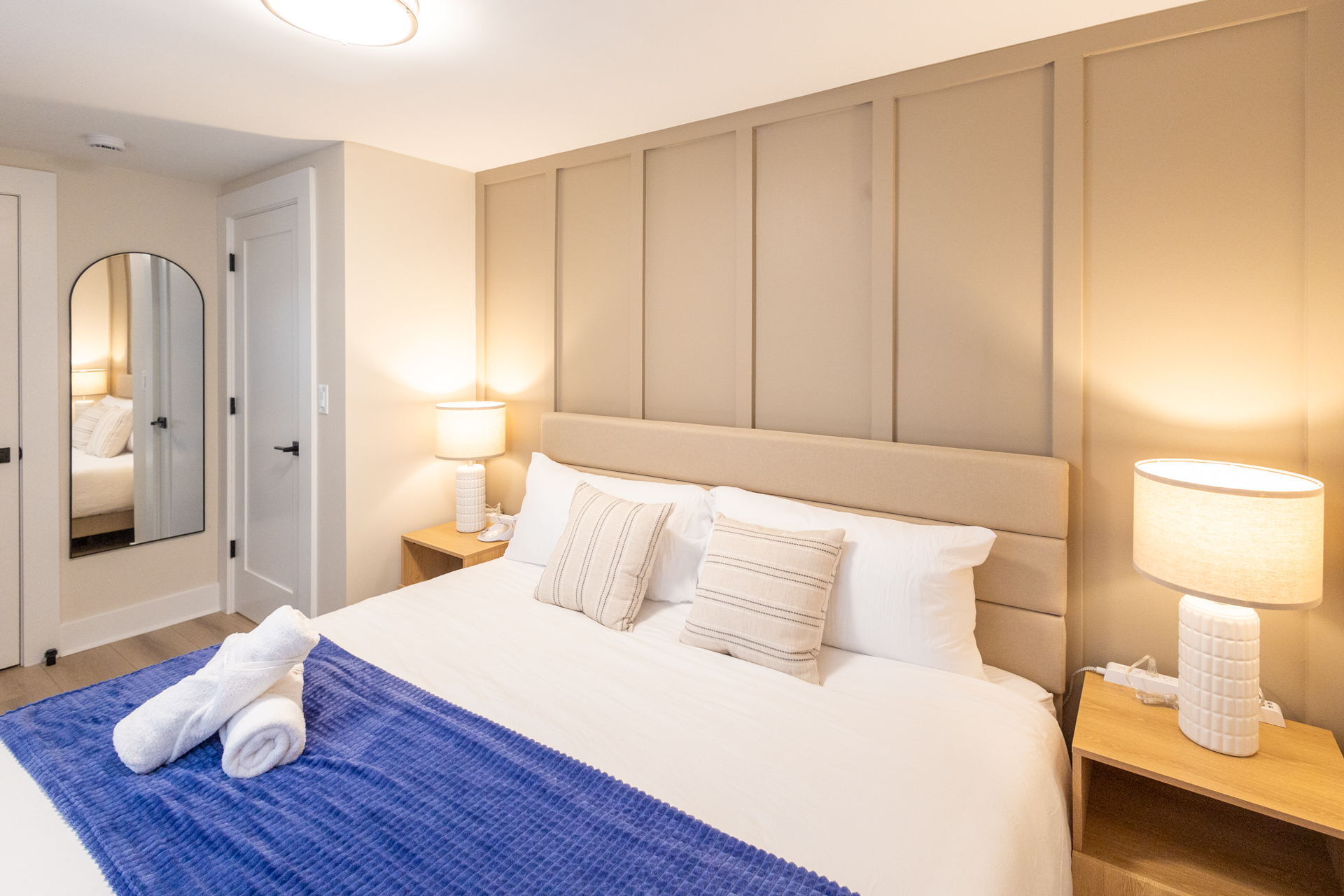Bright bedroom with a king bed, bedside tables, lamps, and a wood-paneled accent wall.