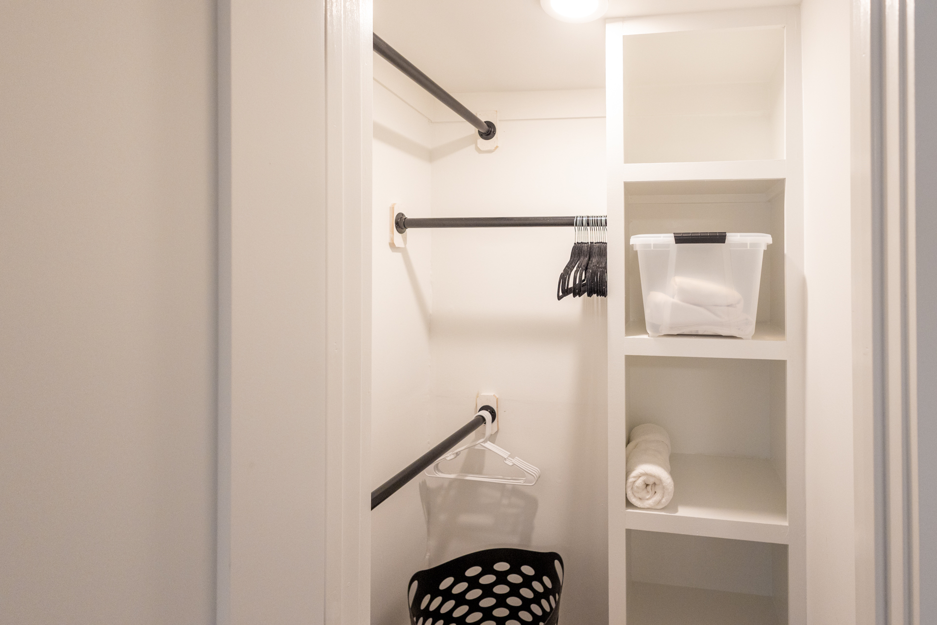Walk-in closet with open shelving, hanging rods, and a laundry hamper.