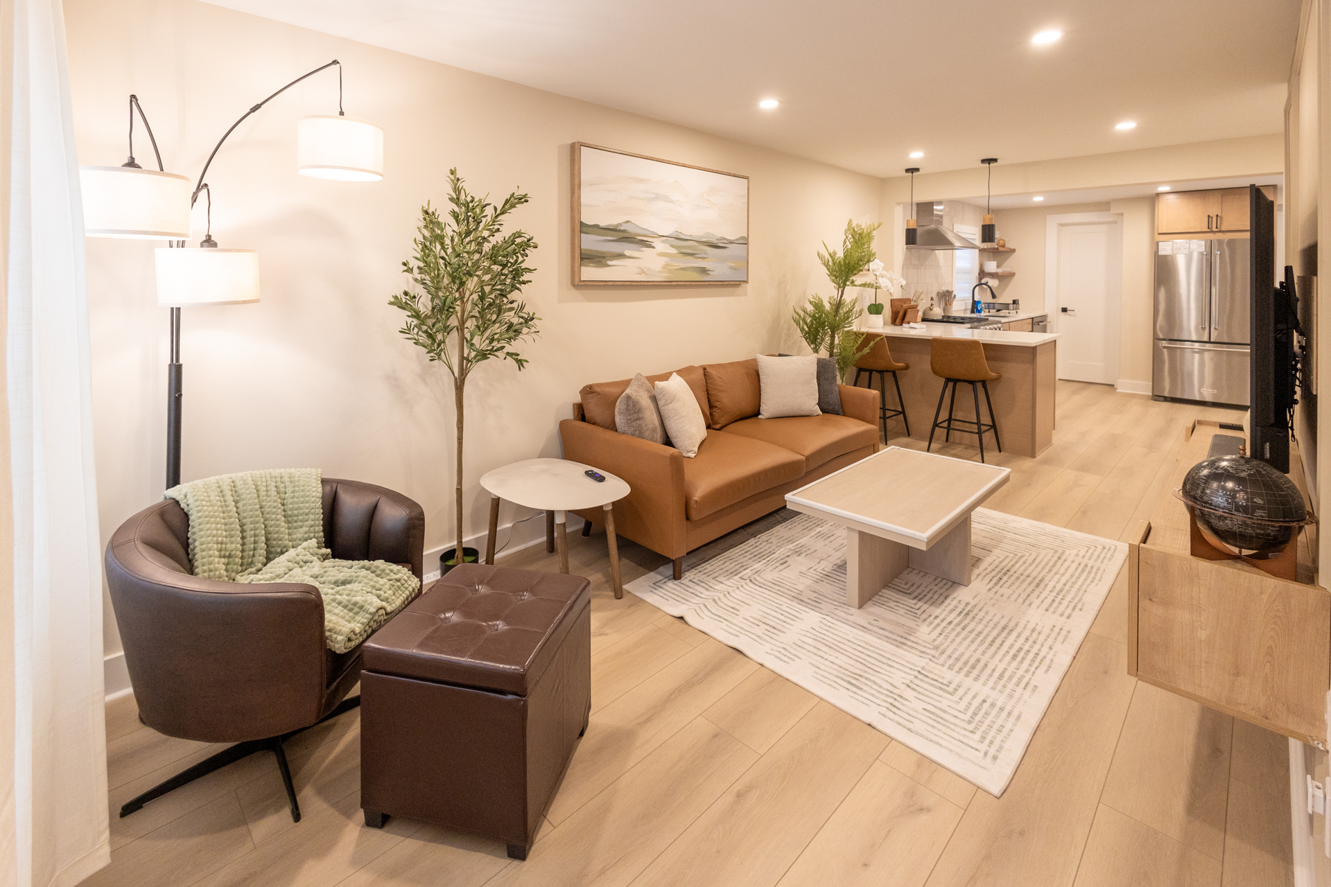 Open-concept living room with a sofa, lounge chair, coffee table, and kitchen in the background.