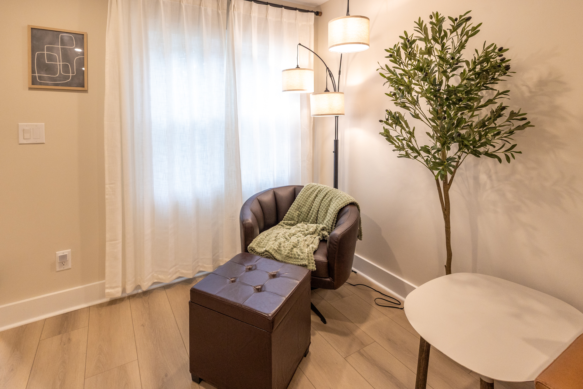 Comfortable sitting area with a leather chair, floor lamp, small table, and potted tree.